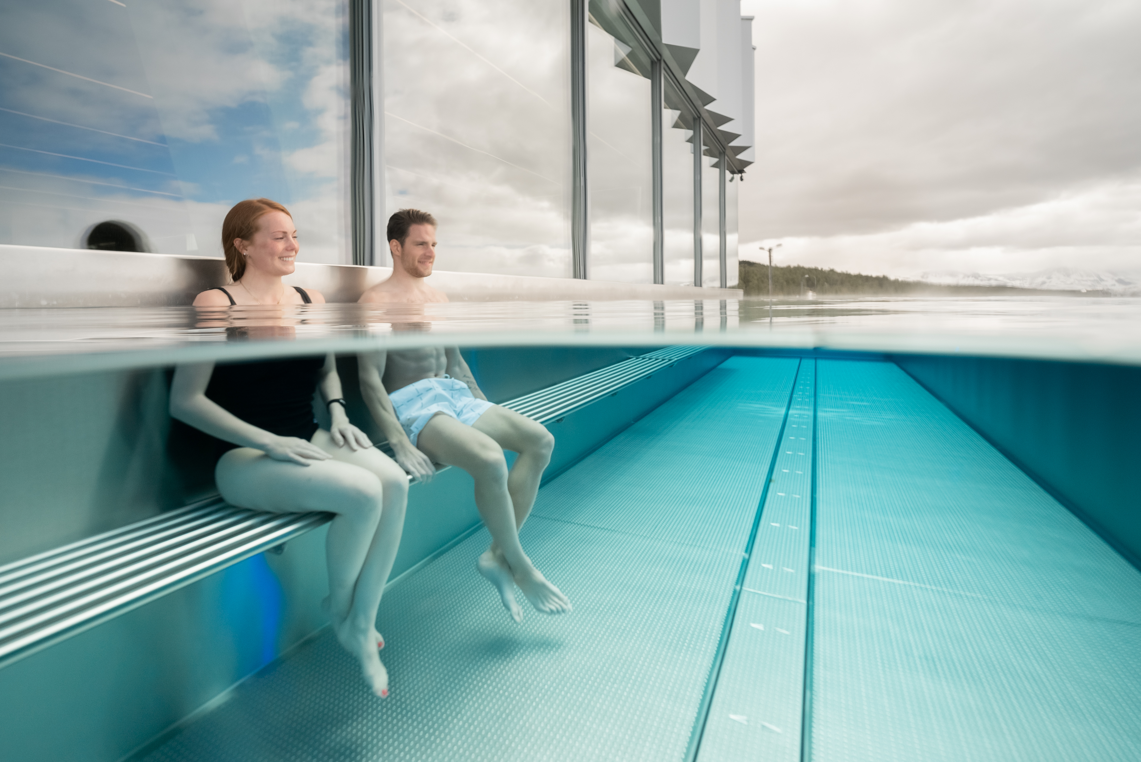 Two guests sitting on a submerged bench in the outdoor pool at Tromsøbadet.